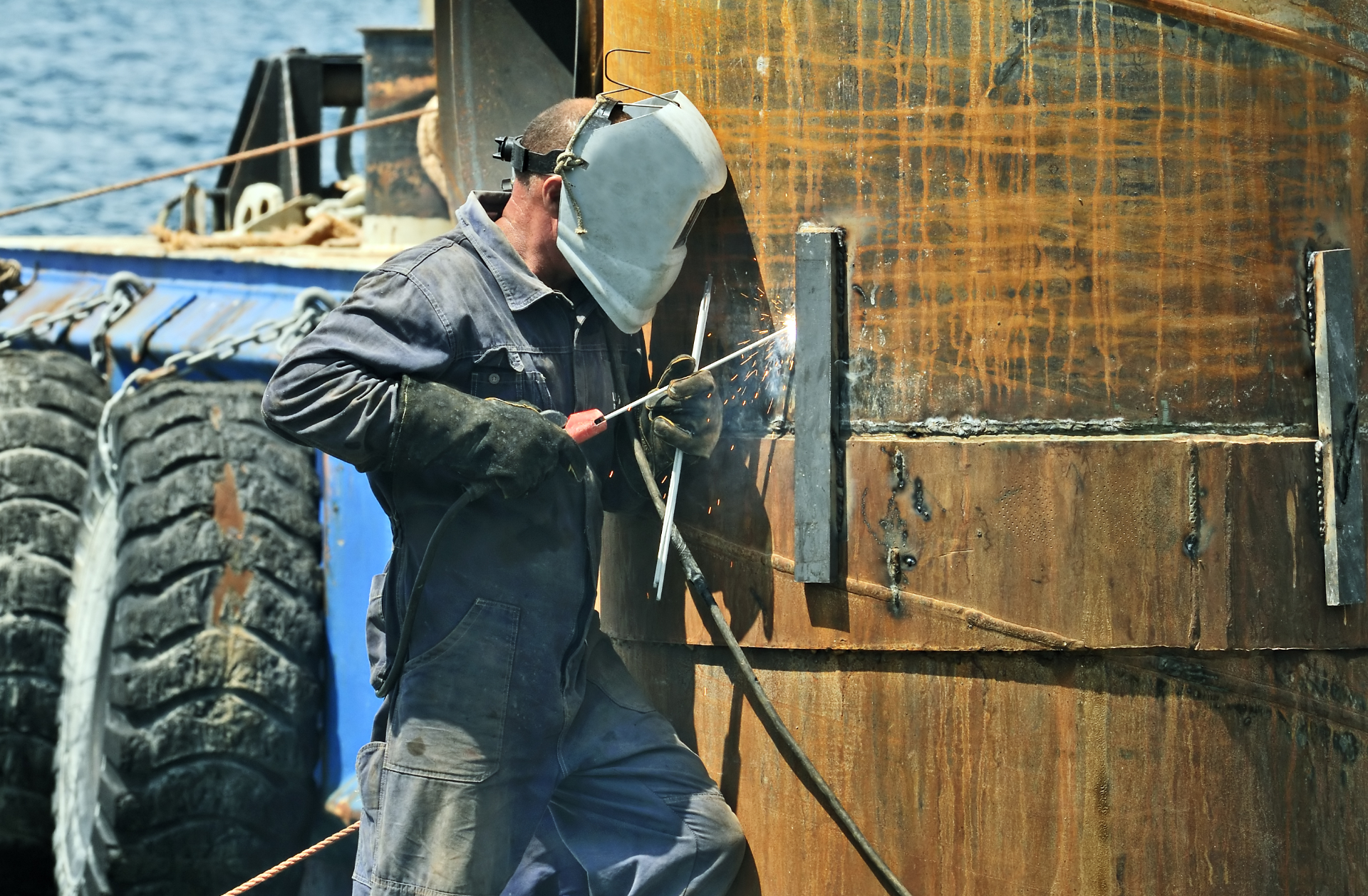 Worker using soldering iron on a rusty pylon in a harbour